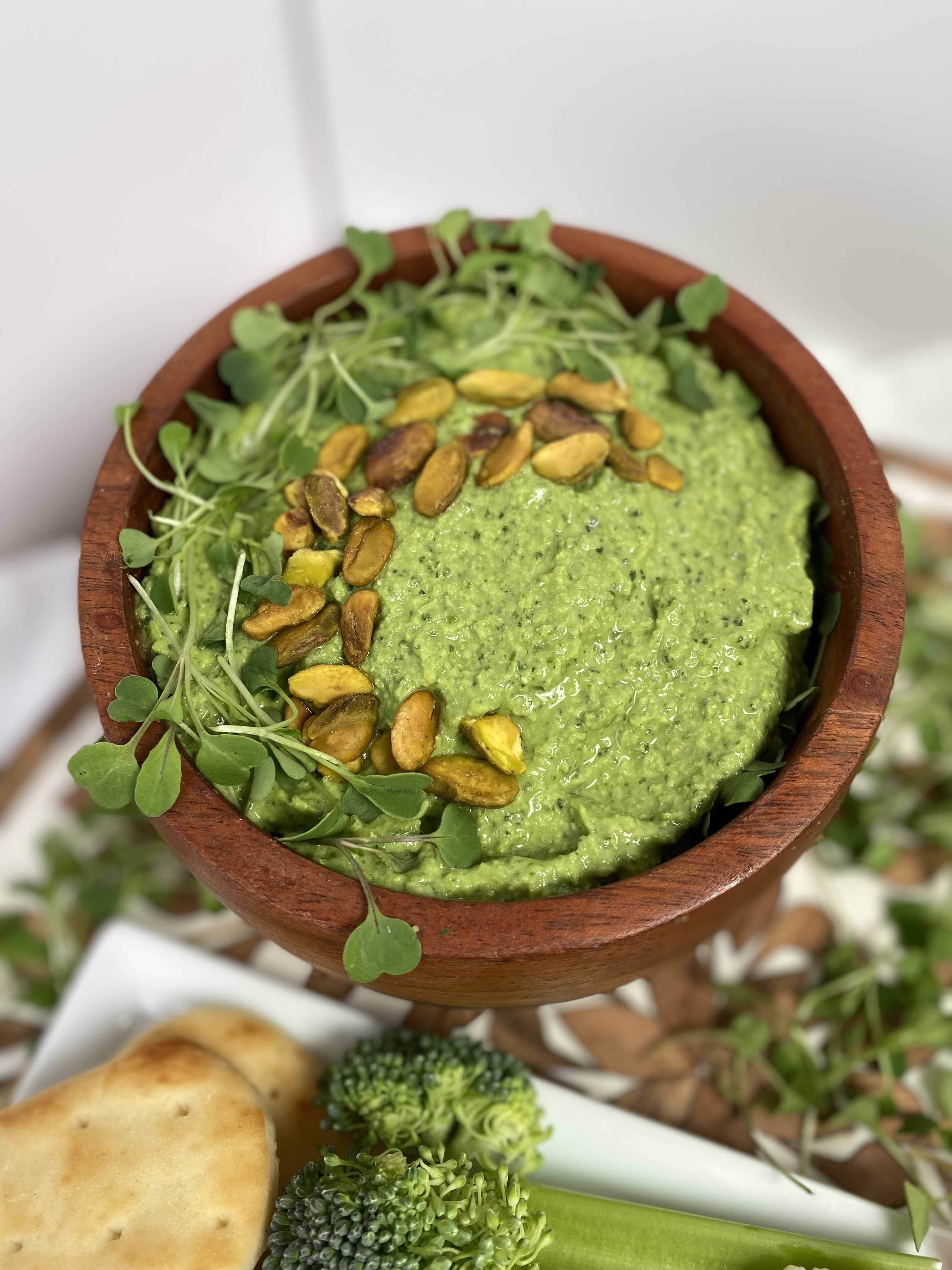 green hummus in wood bowl with pistachios and micro greens garnish