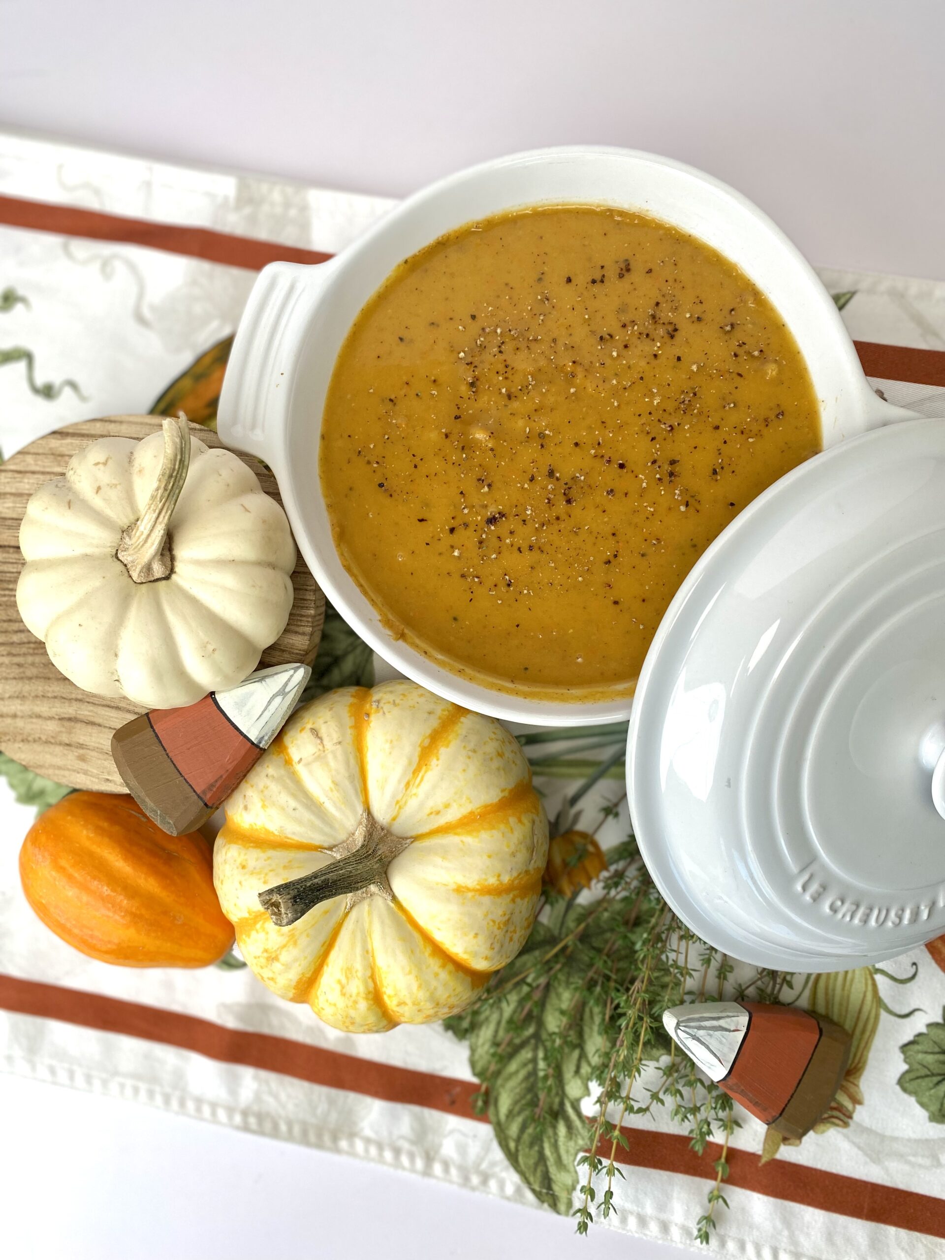 butternut squash soup in white bowl overhead shot next to mini pumpkins on autumn table runner
