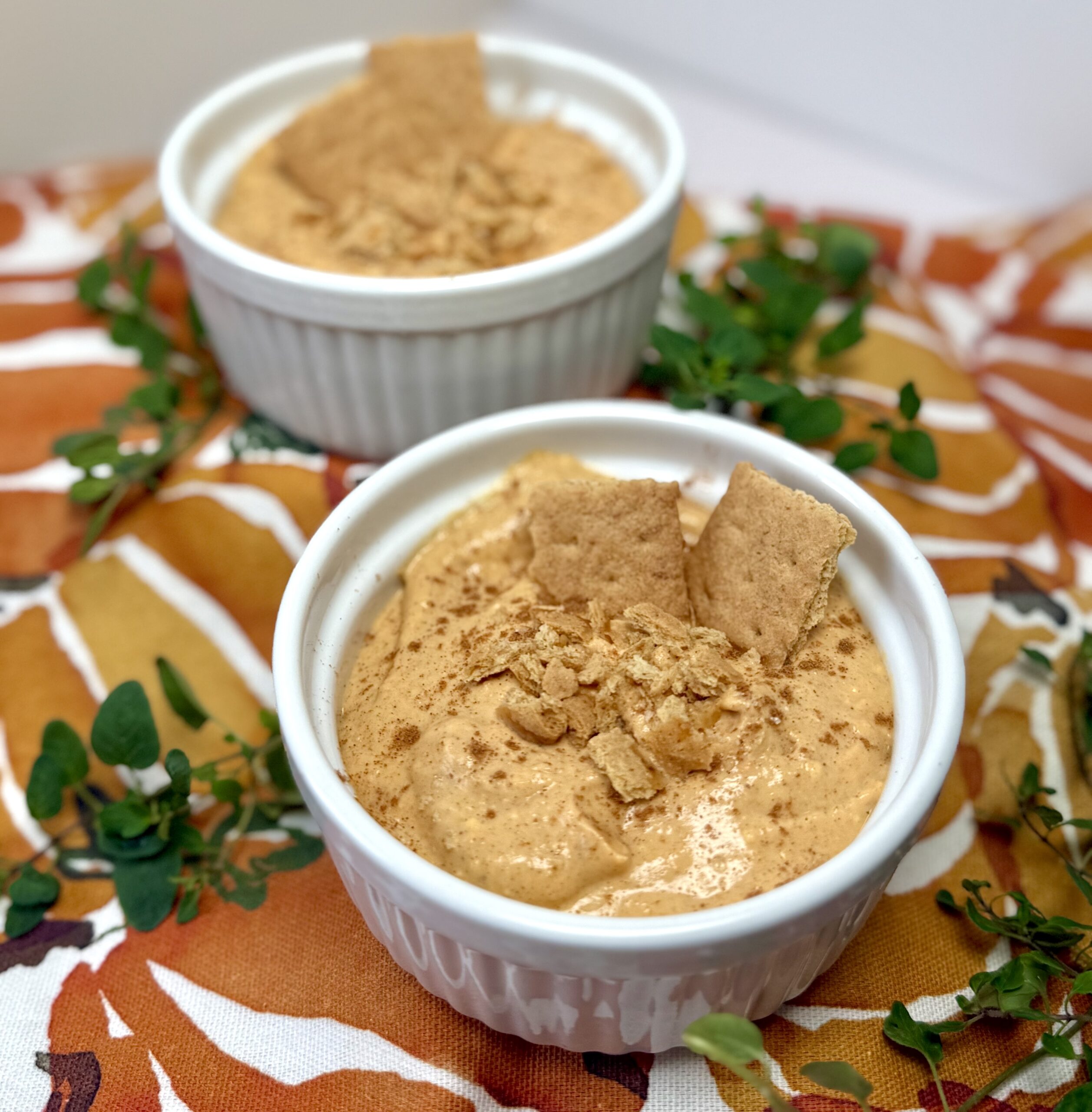 two pumpkin pie ramekins with graham cracker crumble on top over a pumpkin cloth